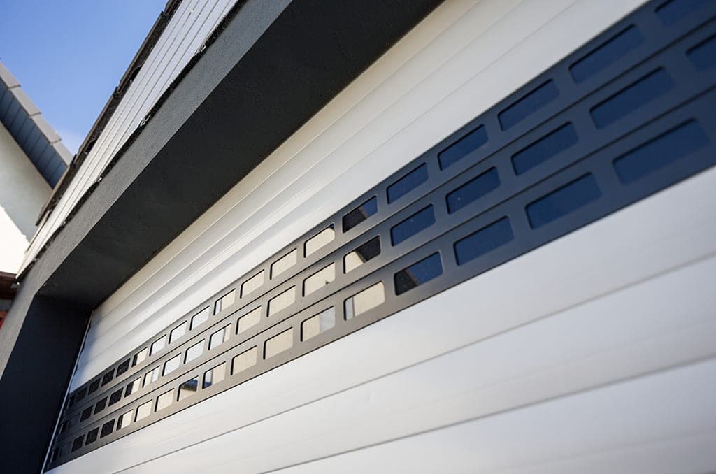 Detailansicht eines weißen Alulux Deckenlauftors mit integrierten Sichtfenstern und Lüftungsprofil.