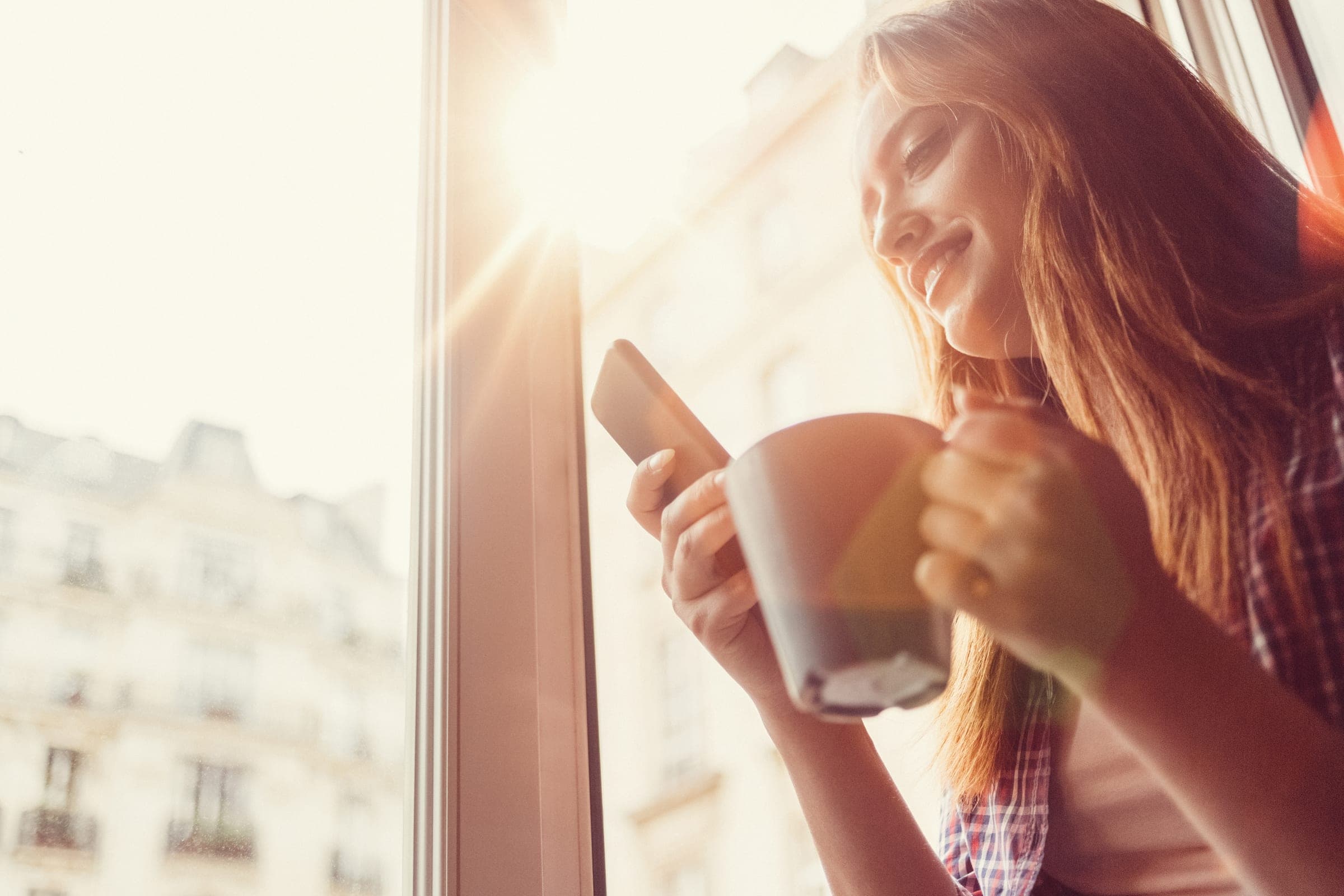 Woman relaxing in the morning sun by the window of a cool living space
