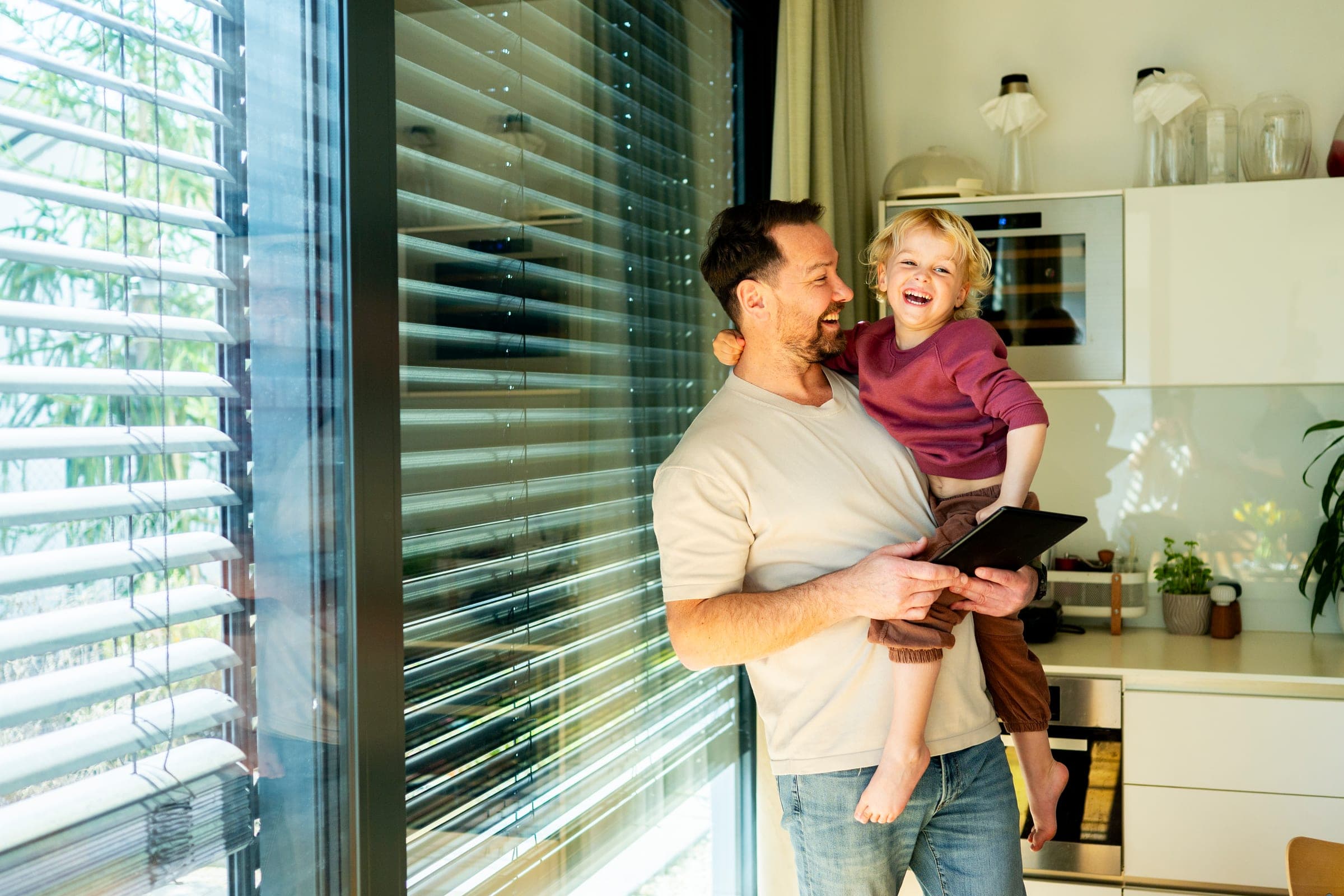 Père et enfant devant une fenêtre ensoleillée avec un raffstore Alulux