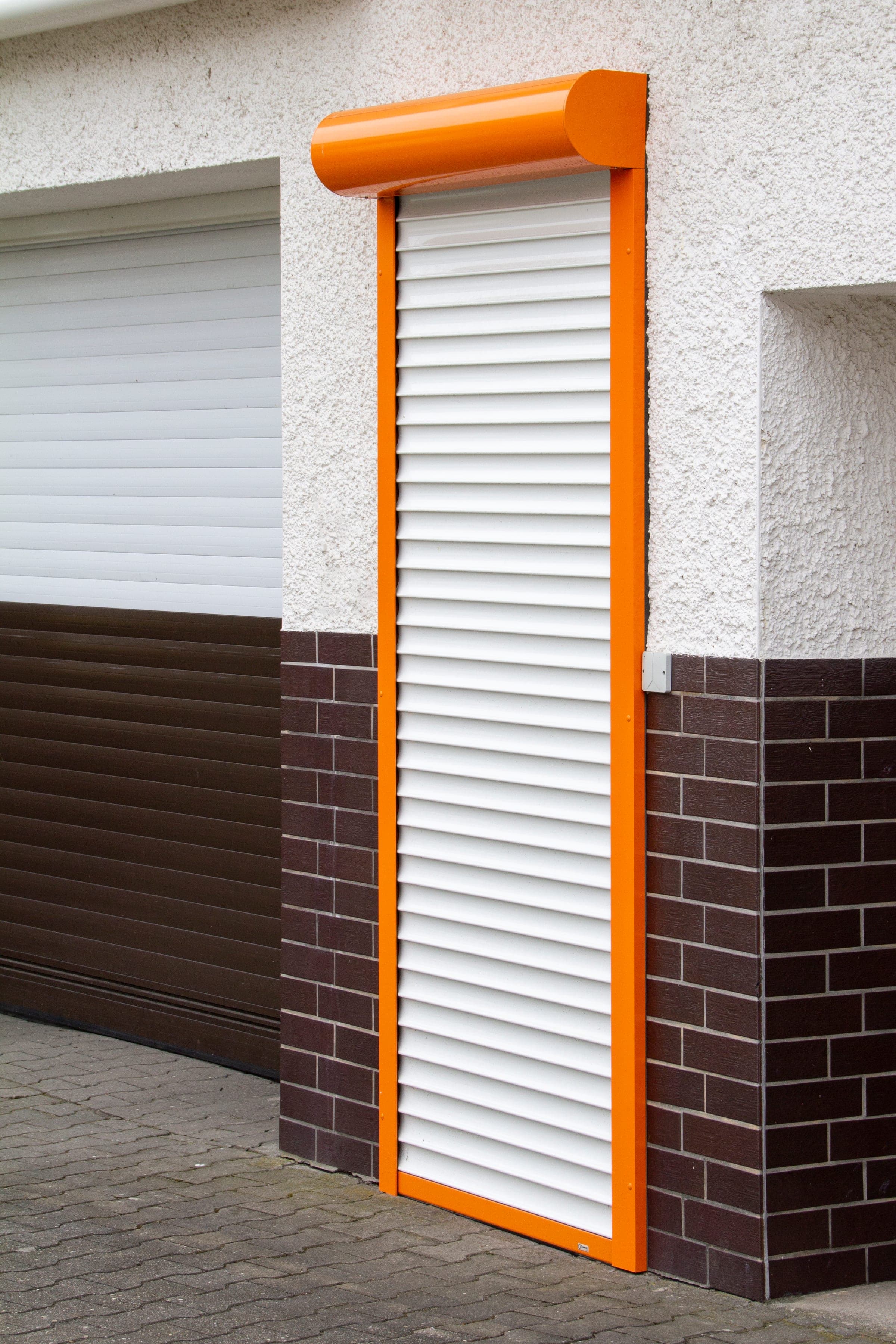 Qompact Sicherheitsrollladen sichert einen schmalen Nebeneingang neben einer Garage