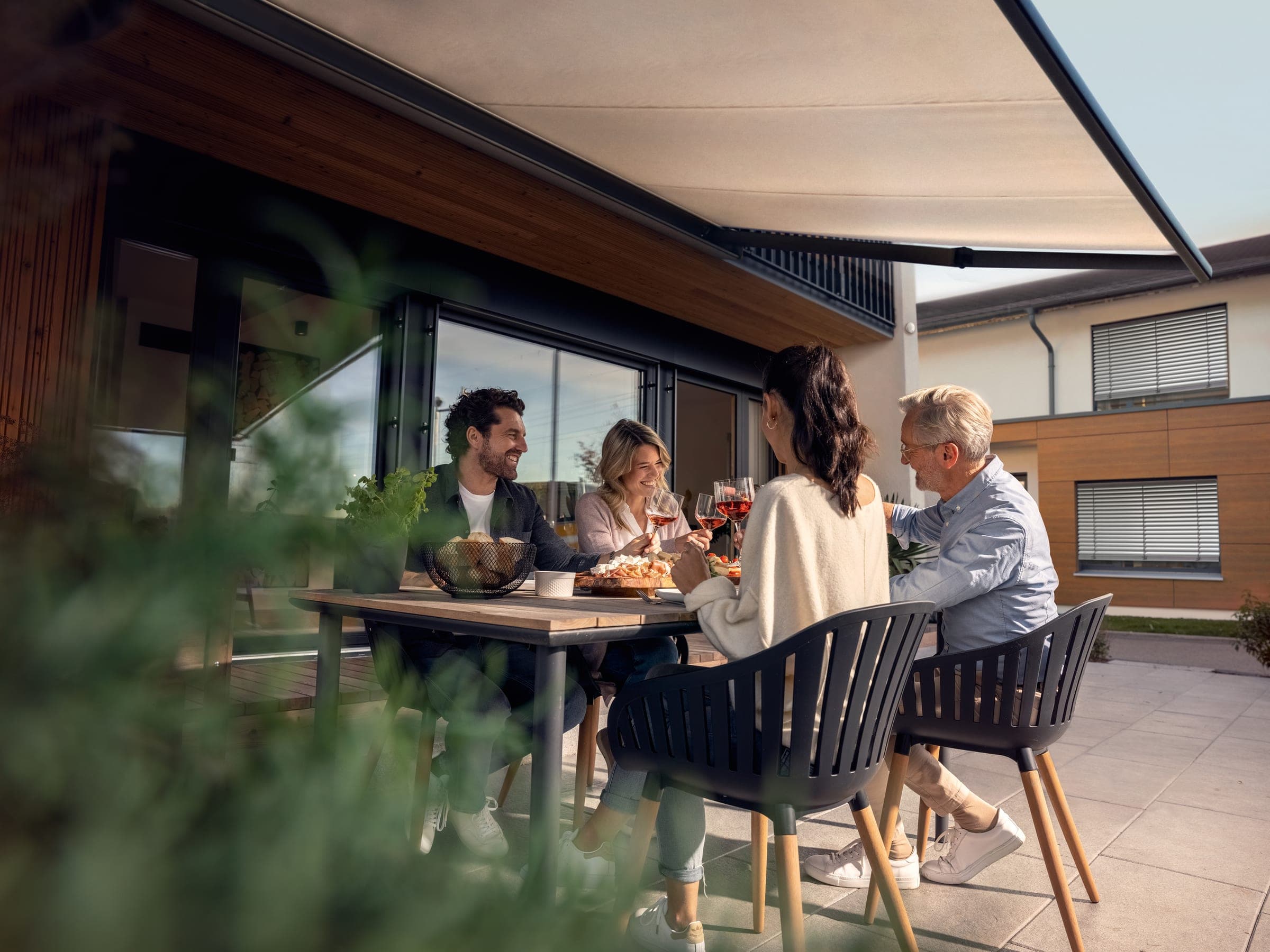 Familie auf einer Terrasse unter automatischer Markise an einem modernen Haus