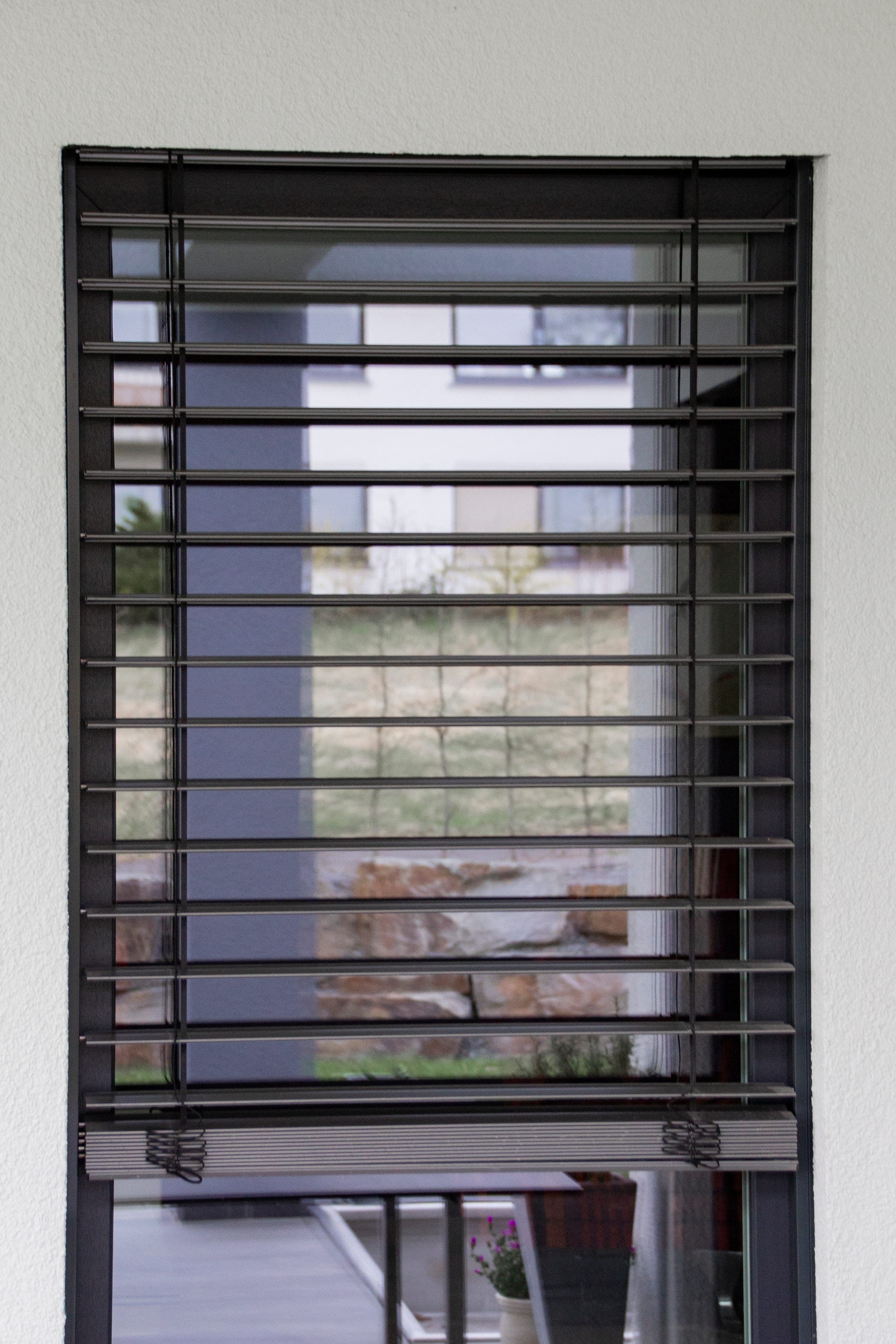 Store vénitien Solo Alulux sur une fenêtre isolée avec vue sur le jardin
