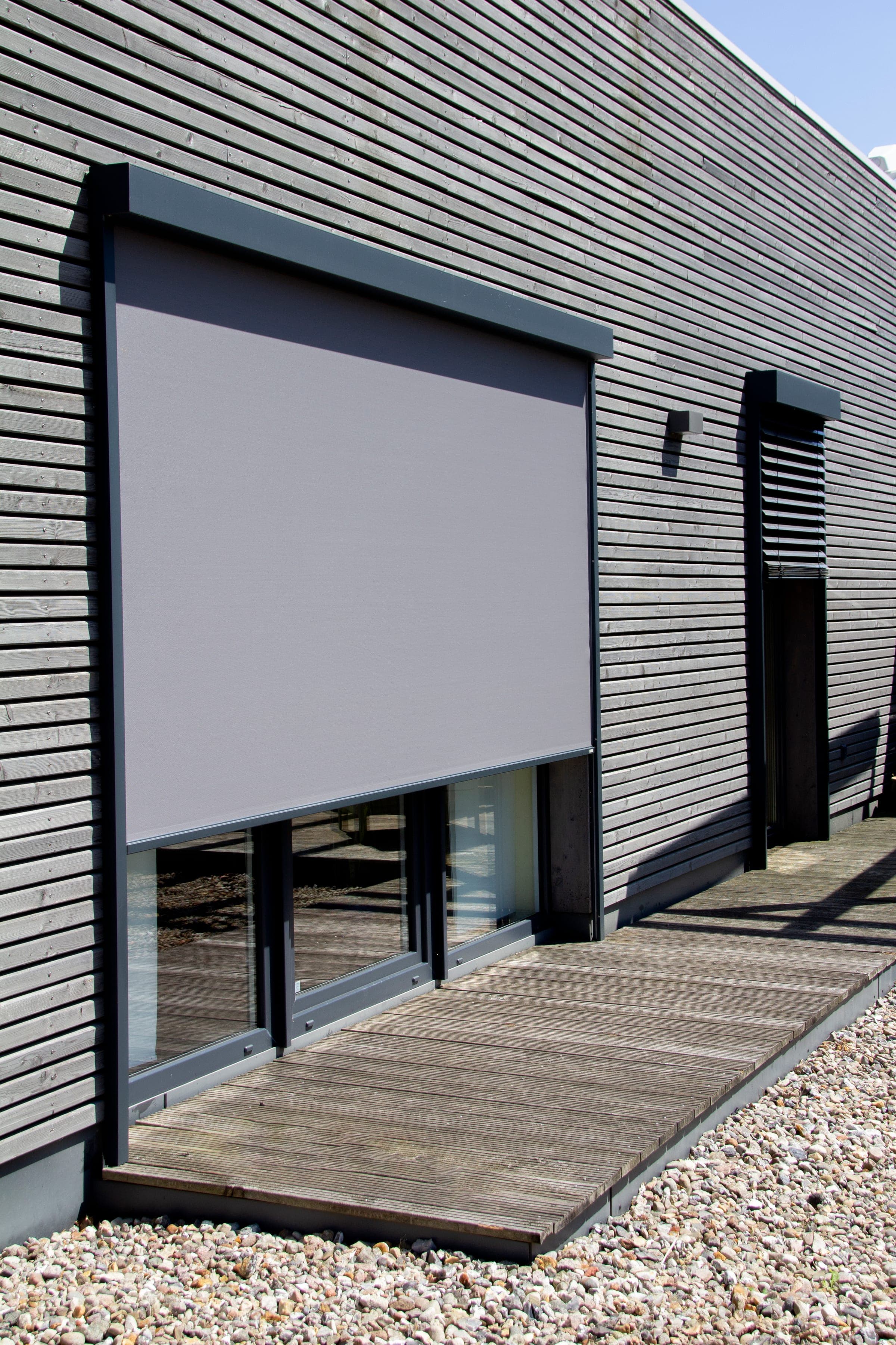 Breite Glasfront mit heruntergelassenem Alulux Vorbau-Textilscreen an einer Holzfassade