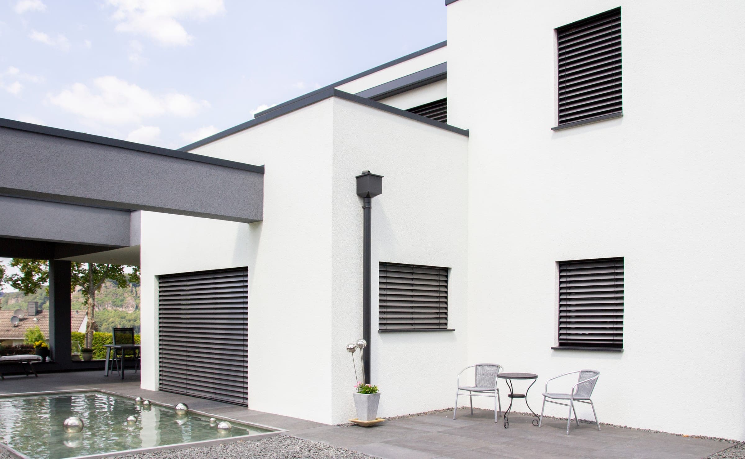 Moderne weiße Fassade mit dunklen Alulux Raffstoren am Pool