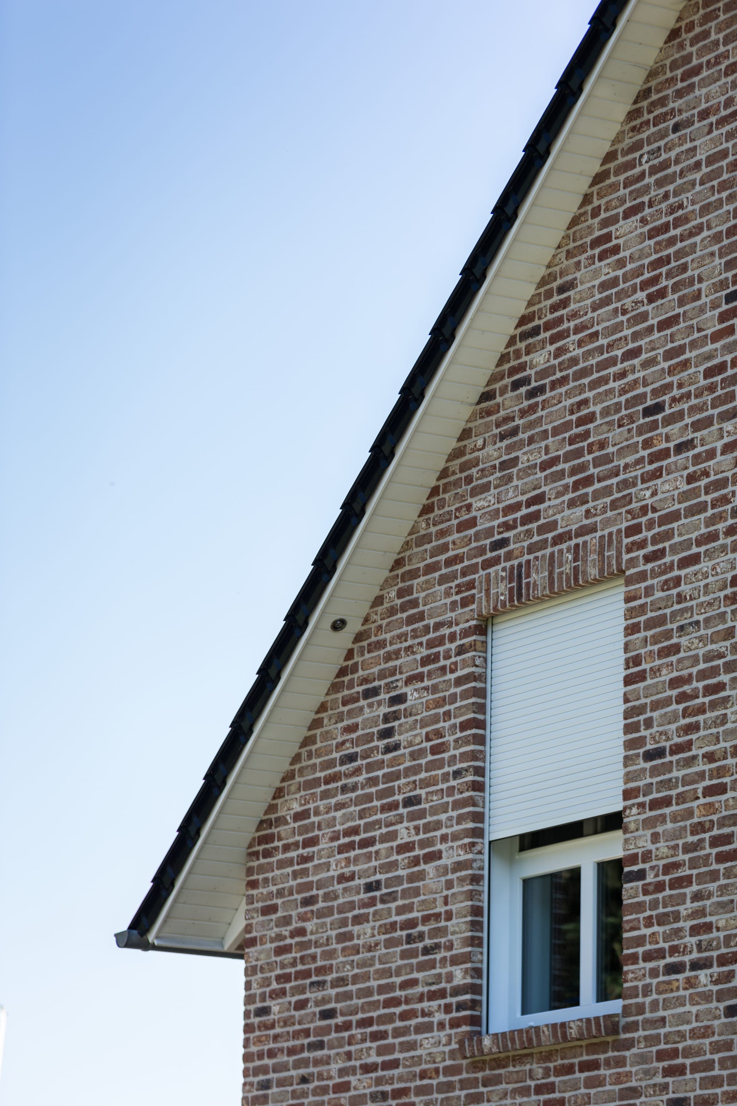 Klinkergiebel eines Einfamilienhauses mit nachgerüstetem weißem Alulux Rollladen am Fenster