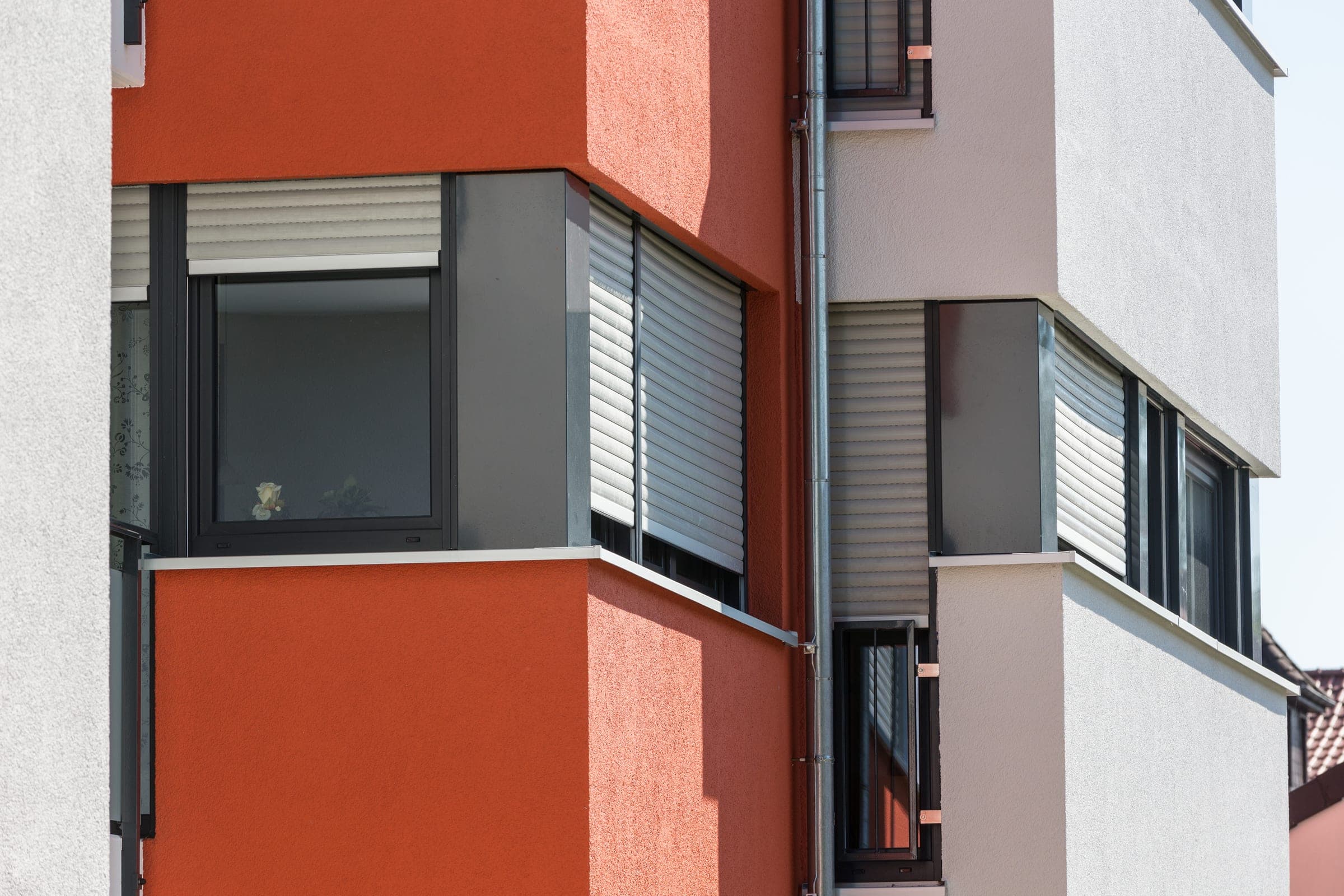 Rotorange verputzte Fassade eines Mehrfamilienhauses mit heruntergefahrenen Alulux Rollladen