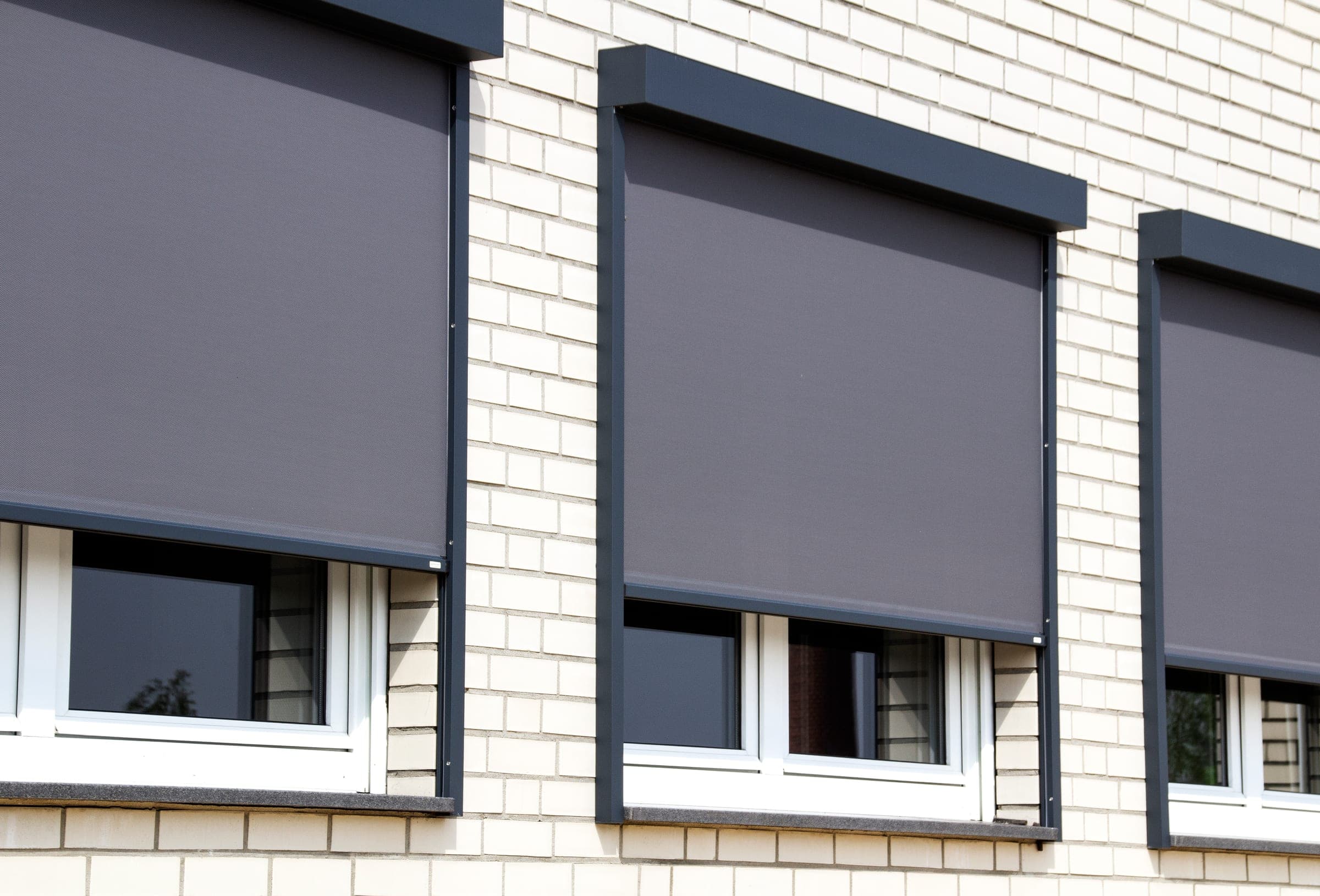 Klinkerfassade mit drei heruntergefahrenen anthrazitfarbenen Alulux Textilscreens in Vorbaukästen