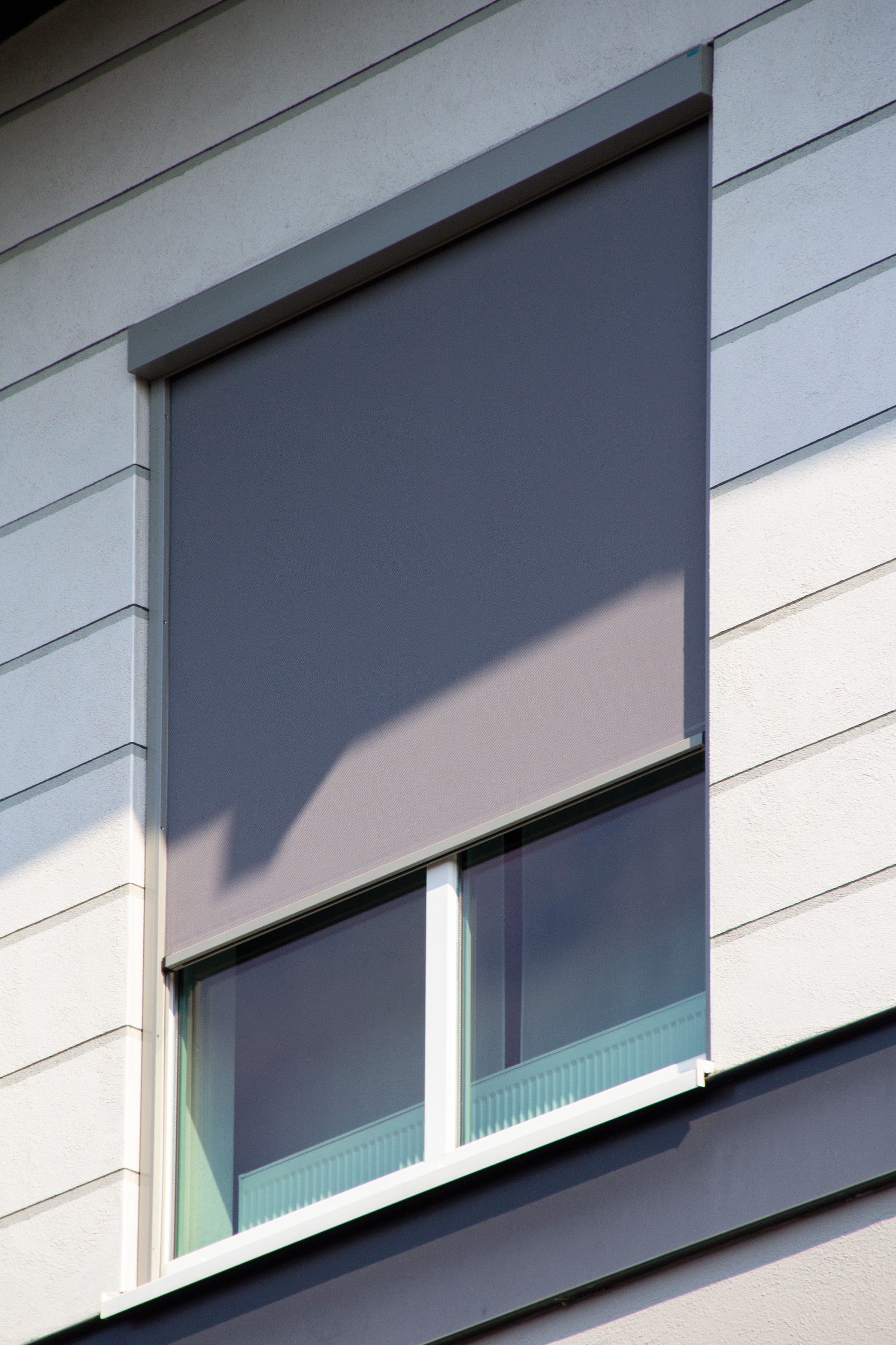 Einzelnes Fenster mit Vorbaukasten und heruntergelassenem Alulux Textilscreen an heller Fassade