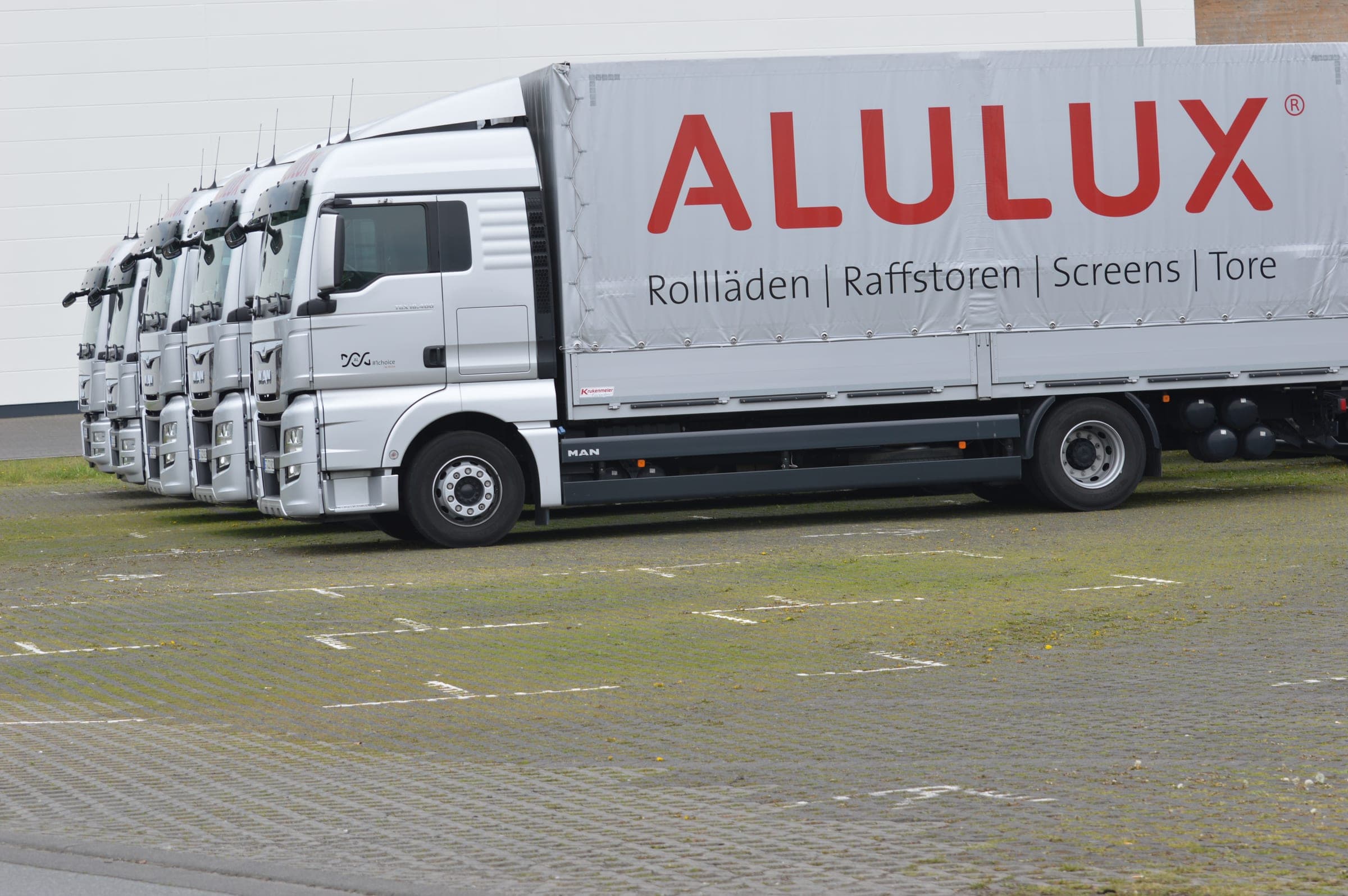 Flotte de camions ALULUX avec l’inscription « Volets roulants | Brise-soleil | Screens | Portes »